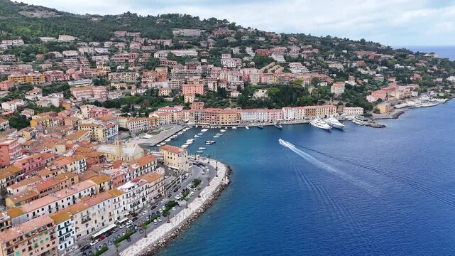 Aerial view of luxury coastal town Porto Santo Stefano with boat sailing to harbor