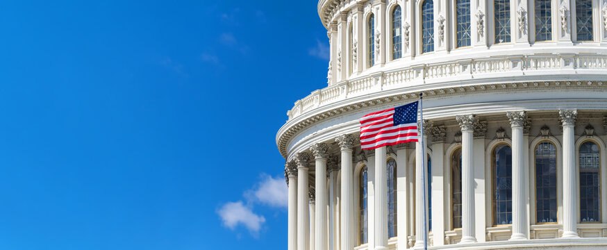Neoclassical architecture of the U.S. Capitol. Dome with flag against a blue sky. Space for text. Washington, D.C.