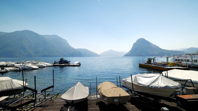 Static shot of boats moored in Lugano marina with Lake Lugano and Monte San Salvatore peak