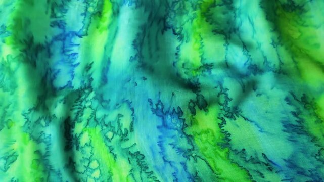 Natural silk fabric with blue and green abstract pattern waving in the wind. Smooth textile surface creating flowing waves and motion background. Abstract turquoise and lime colored silk material.