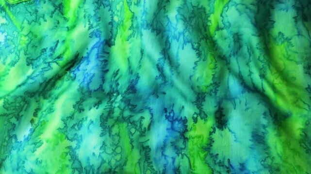 Blue and green abstract silk fabric waving in the wind. Smooth flowing natural silk textile creating soft ripples and waves. Seamless motion of turquoise and lime colored fabric background.
