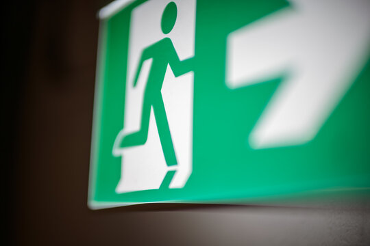 Close-up of green emergency exit sign with running figure and directional arrow on indoor wall, safety evacuation guidance in building corridor