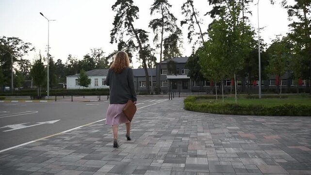 Slow motion back view of a young blonde woman walking across an empty parking lot. Bright sunlight creates a minimal urban lifestyle scene with a sense of space and movement.