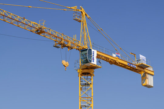 Mirecourt, France - March 21st 2026 : View on a yellow hammerhead top-slewing tower crane Potain MD 265 B1 J10 on a construction site for the construction of a building with the blue sky.	