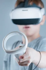 A gamer wearing virtual reality glasses with controllers and a headset © Alexander