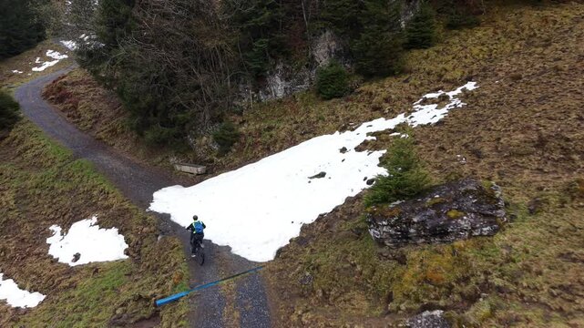 Drone follow shot of a cyclist climbing a hill and crossing a small remaining snow patch on a mountain road