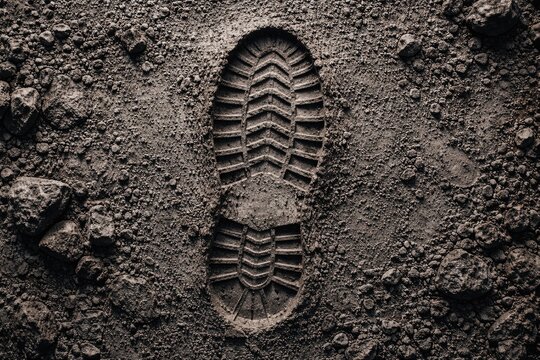 Exploration themed boot print on rugged gray terrain texture in flat lay format