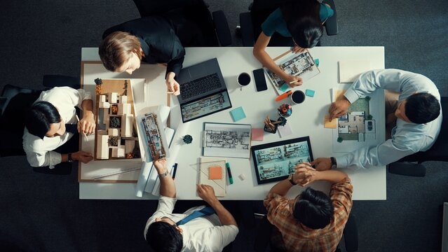 Architect team discussing and pointing and presenting blueprint to interior designer. Aerial view professional business people brainstorming building interior at table with house model. Alimentation.