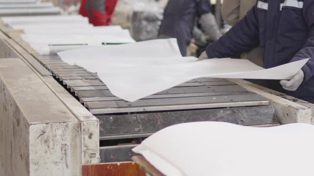 Factory workers hands folding and arranging white material on conveyor belt, meticulously preparing products for distribution in an industrial environment