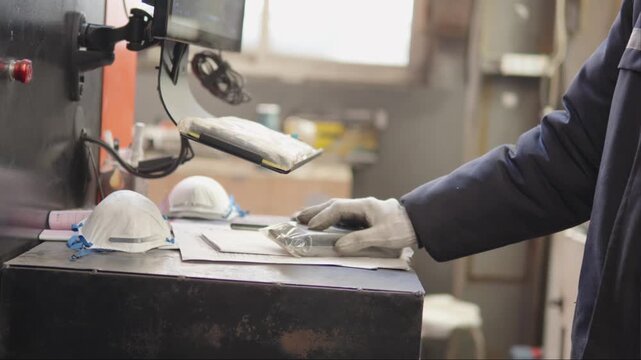 Industrial worker putting an item for processing into an operating machine in a factory, showing the continuous hard work, production, and manufacturing process