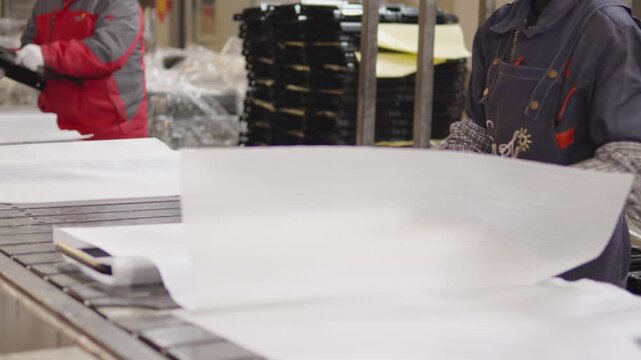 Factory workers on active assembly line carefully wrap industrial products in protective paper, securing packaging and quality control for safe shipment in a modern facility