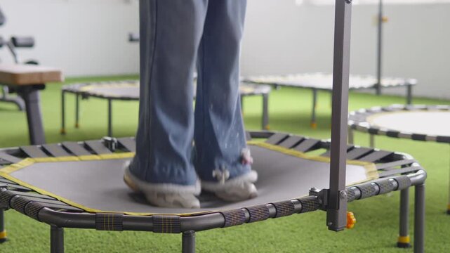Young girl children in jeans and sneakers jumping on mini rebounder trampoline indoors, close up of legs in motion for cardio, balance and fun home workout routine