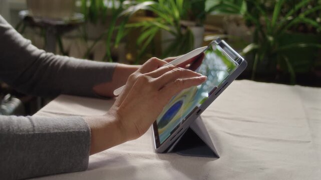 Woman drawing a picture on a tablet screen while sitting in a room at a table