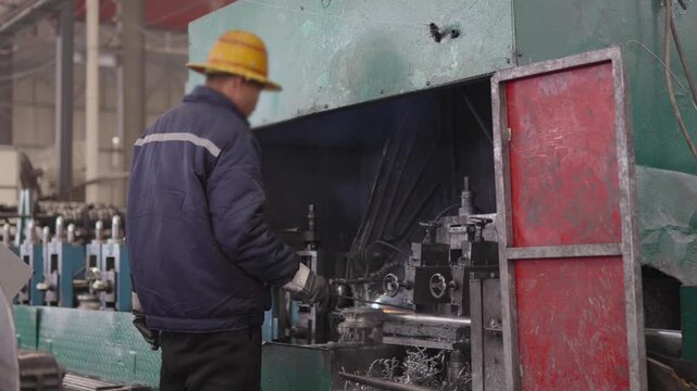 Factory worker in protective gear operating a large industrial machine in a manufacturing plant, actively engaged in machine working and industrial production