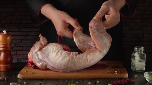Chef prepares rabbit raw meat on wooden cutting board, focusing on handling and positioning the meat with visible kitchen tools and ingredients in the background