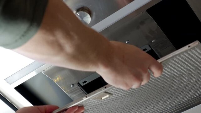 Close up of person replacing metal grease filter in kitchen hood. Concept of appliance cleaning and household maintenance