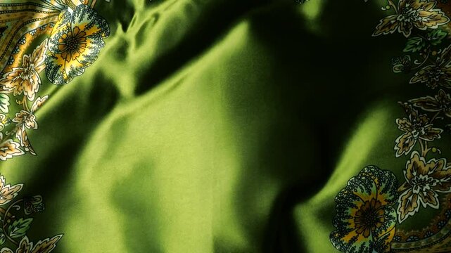 Natural silk fabric with floral pattern fluttering in the wind. Green textile material creates abstract waves background. Detailed view of flowing smooth cloth with yellow flowers ornament.