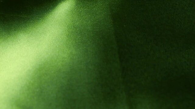 Green natural silk fabric fluttering in the wind. Abstract background with soft waves and flowing textile. Elegant emerald color with smooth satin texture. 