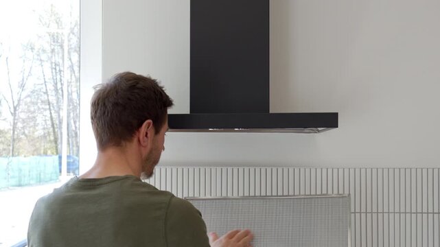 Person removes metal filter from black kitchen hood in modern home interior. Concept of appliance cleaning, household maintenance and kitchen care.