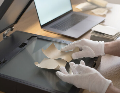 Hands carefully arrange old photos on a scanner bed. A person digitizes vintage paper prints, preserving history. Modern technology captures past images for a digital archive.