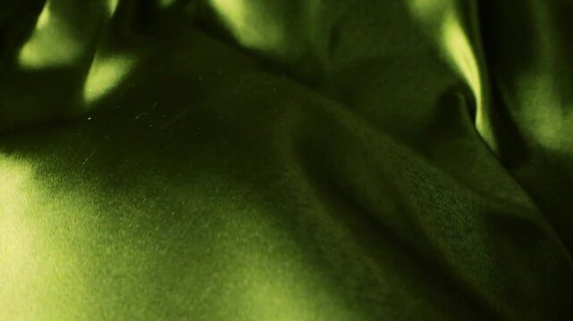Abstract background of natural silk fabric waving in the wind. Flowing olive green and yellow textile material with soft waves. Smooth satin cloth surface with blurry organic shapes and shadows.