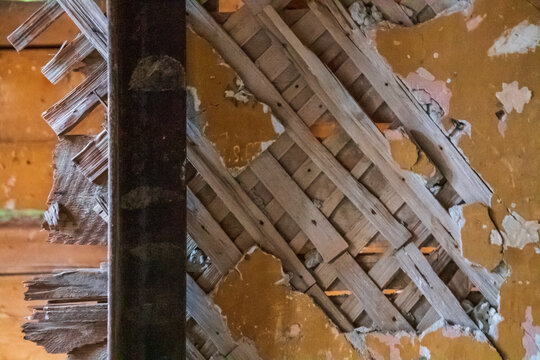 Peeling yellow plaster exposes a diagonal wooden lath structure behind an old interior wall, evoking rustic decay, tactile texture, and the need for repair or renovation in an abandoned building.
