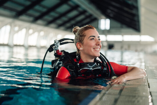 Woman diver smiling in swimming pool, preparing for scuba diving training, wearing wetsuit and dive gear
