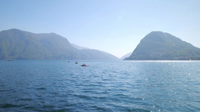 Panning shot of Lake Lugano with pedal boats and misty mountains in the background, Switzerland