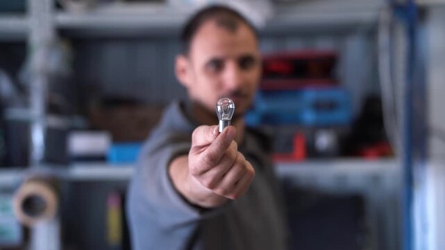 A man shows off a new car light bulb in a garage, auto repair shop and repair shop.