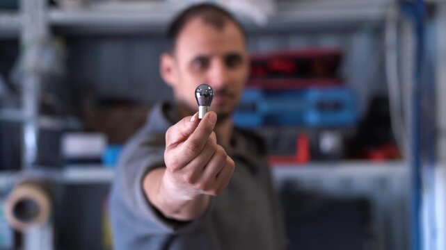 Man holding car burned out black light bulb in workshop, repair and maintenance concept.