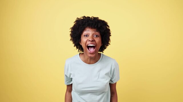 Young woman expressing surprise and excitement on yellow background