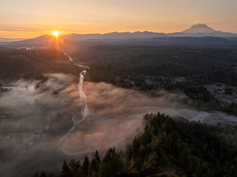 Aerial view of the Foothills Trail shrouded in ethereal mist, the sun's golden rays kissing the peaks of distant mountains, Orting, Washington, United States.