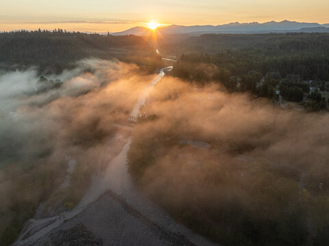 Aerial view of the Foothills Trail river obscured by a soft blanket of fog under the warm glow of the rising sun, Orting, Washington, United States.