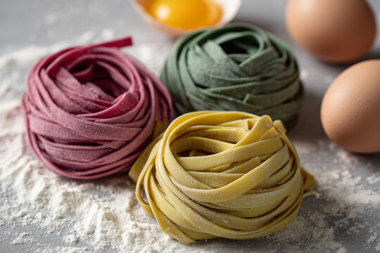 Homemade assorted naturally dyed pasta nests close up with Italian ingredients around. Meal prep and recipe cooking concept.