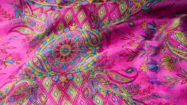 Silk fabric with pink paisley pattern waving in the wind. Abstract background of moving natural silk material with floral ornaments. Bright pink textile with colorful eastern print creates soft waves.