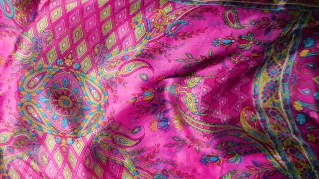 Natural silk fabric with paisley patterns waving in the wind. Abstract background featuring waves of pink and multicolored floral textures. Bright fuchsia and traditional oriental motifs.