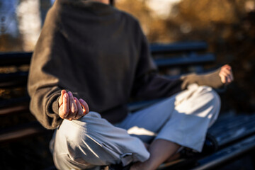 Fototapeta premium Close up of hands and legs in meditation pose on park bench