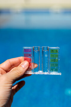 Close-up of a hand holding a pool water testing kit with color scale, measuring pH and chlorine levels in a clear blue swimming pool outdoors - pool maintenance concept