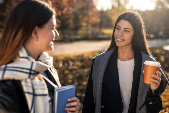 Two college girls holding books and takeaway coffee spending time together