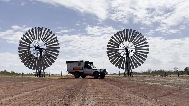 Off road vehicle parked between giant wind turbine blades in Northern Territory, Australia. Unique outback scene combining renewable energy, industry, and remote landscape.