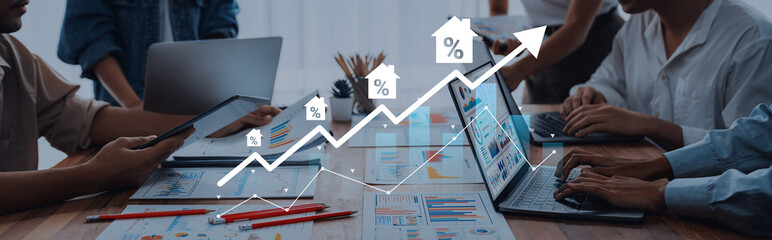 Naklejka premium A group of professionals engages in a detailed discussion about real estate market trends, analyzing data on laptops while using charts to visualize growth and insights. Gantry