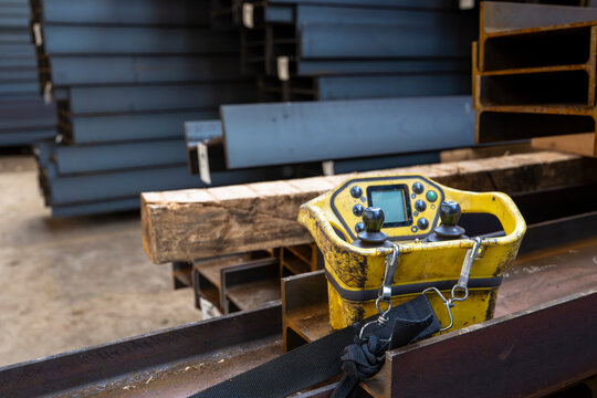 Industrial crane remote control unit placed on steel beam inside warehouse showing equipment used for operating heavy lifting systems in manufacturing environment