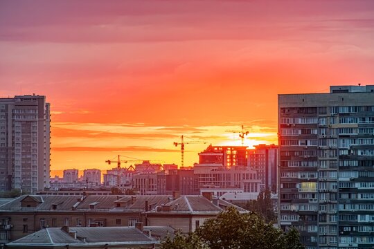 Sunset panorama of Kyiv cityscape with warm orange glow, residential buildings, architectural features, mixed building heights, high vantage point, horizon line, cool contrasting tones, rule of third