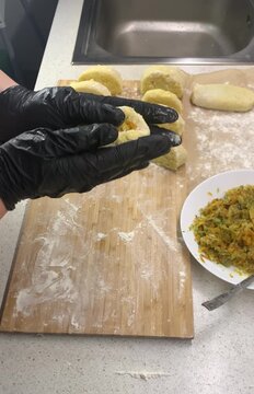 Close-up of a chef in black gloves stuffing potato dough with fried cabbage to make traditional Zrazy. Cooking process on a wooden board sprinkled with flour.