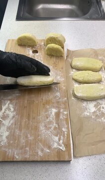 Close-up of a chef in black gloves stuffing potato dough with fried cabbage to make traditional Zrazy. Cooking process on a wooden board sprinkled with flour.
