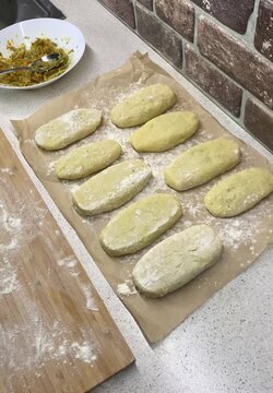 Close-up of a hand in a black nitrile glove adding the last raw patty to a row on parchment paper. Final step of food preparation and shaping. Professional kitchen workflow, meal prep, and handmade