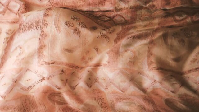 Natural silk fabric with abstract geometric pattern flowing in the wind. Light brown and beige textile ripples creating soft waves and shadows. Elegant silk material with symmetrical shapes.