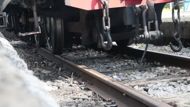 Plano detalle de las ruedas, cadenas de enganche y sistema de acoplamiento de una locomotora de vapor cl&aacute;sica detenida sobre las v&iacute;as en una estaci&oacute;n.