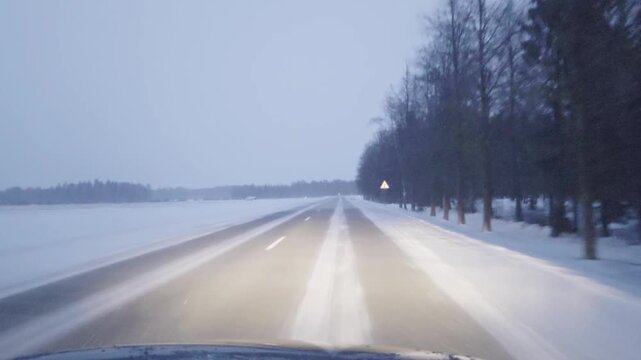 Night Driving in Lithuania During Winter Storm: Car Navigating a Snowy and Slippery Regional Road Amidst Falling Snow and Low Visibility.
