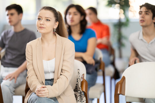 Focused young girl sitting and listening to lecture together with others in training room